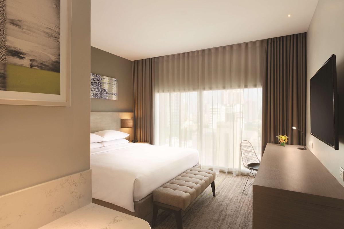 A modern hotel room with a large bed, a desk, and a TV.