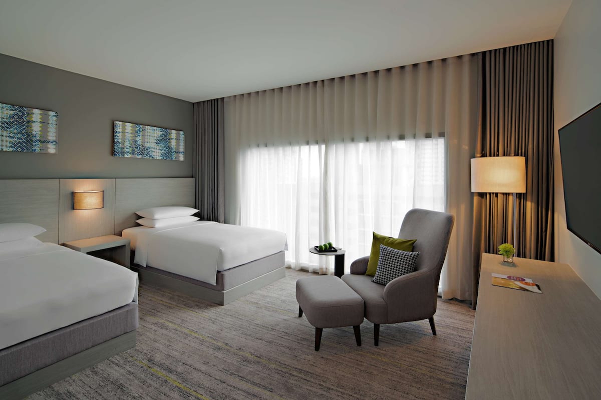 Une chambre d’hôtel avec deux lits, un canapé, un fauteuil, une télévision et des œuvres d’art accrochées aux murs.