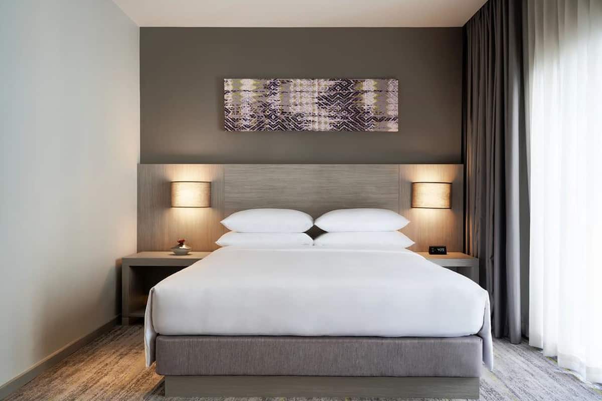 Une chambre d’hôtel moderne avec un grand lit, deux tables de chevet et une œuvre d’art abstraite accrochée au mur.