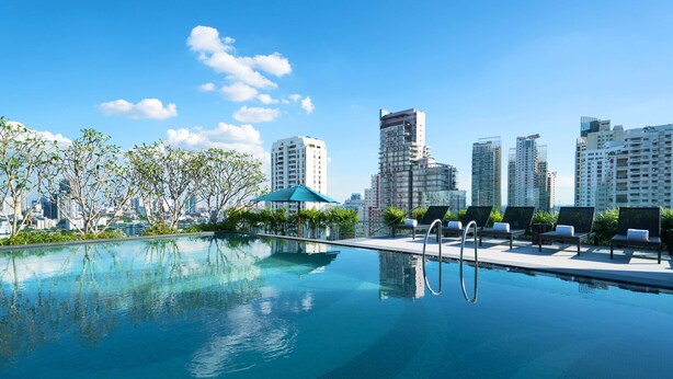 Piscina infinita en la azotea con sillones de descanso y vistas a un horizonte urbano.
