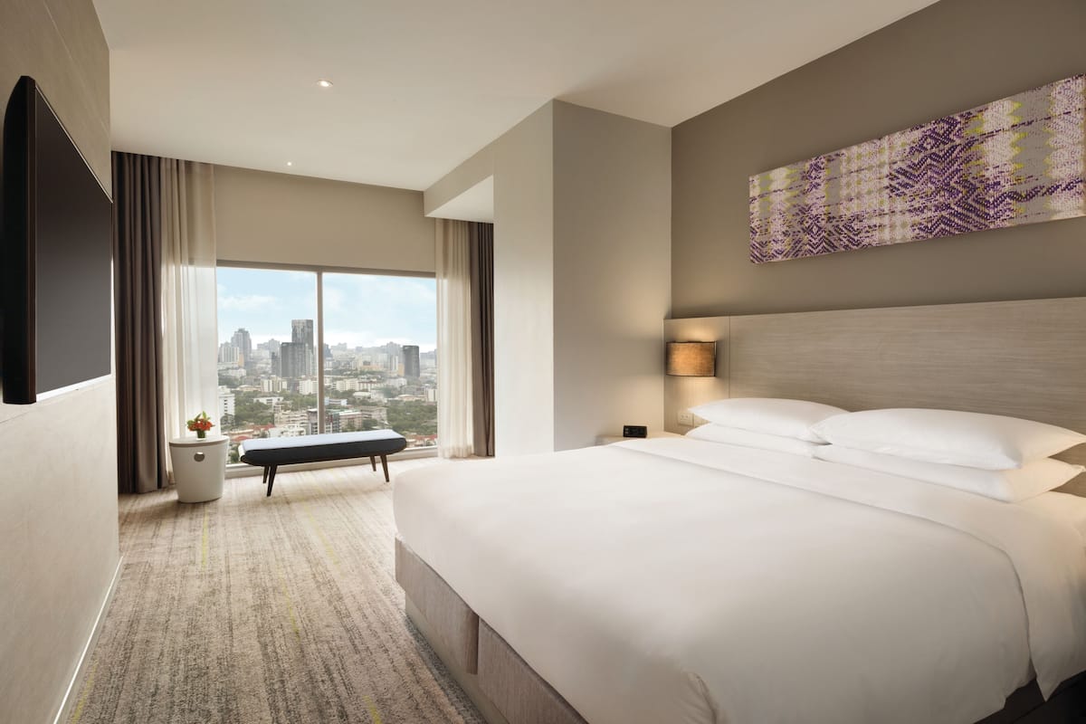 Une chambre d’hôtel moderne dotée d’un grand lit, d’une vue sur la ville, d’un téléviseur à écran plat et d’un élément décoratif mural.