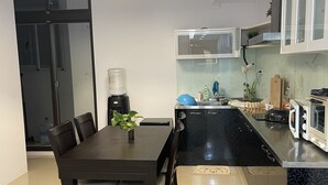 A modern kitchen with a dining area, featuring a dark wooden table, chairs, a hanging light fixture, and a water dispenser. - Keyinn Space (Hualien City)