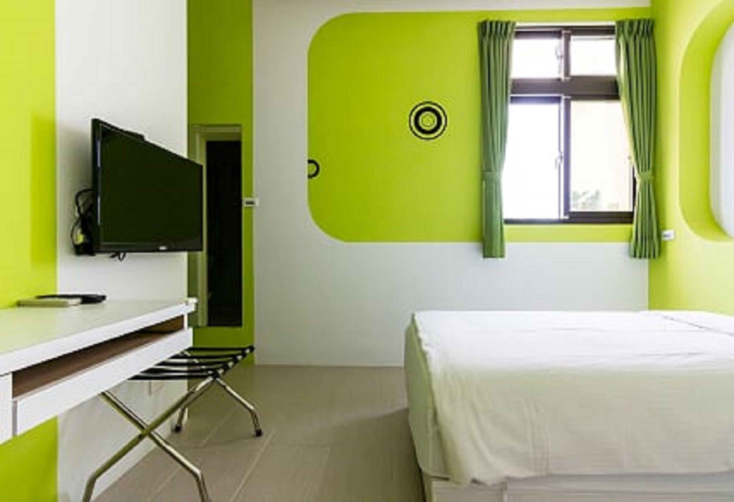 Ein Zimmer mit einem Bett, einem Schreibtisch mit Stuhl, einem Fernseher und einem Fenster mit Vorhängen.