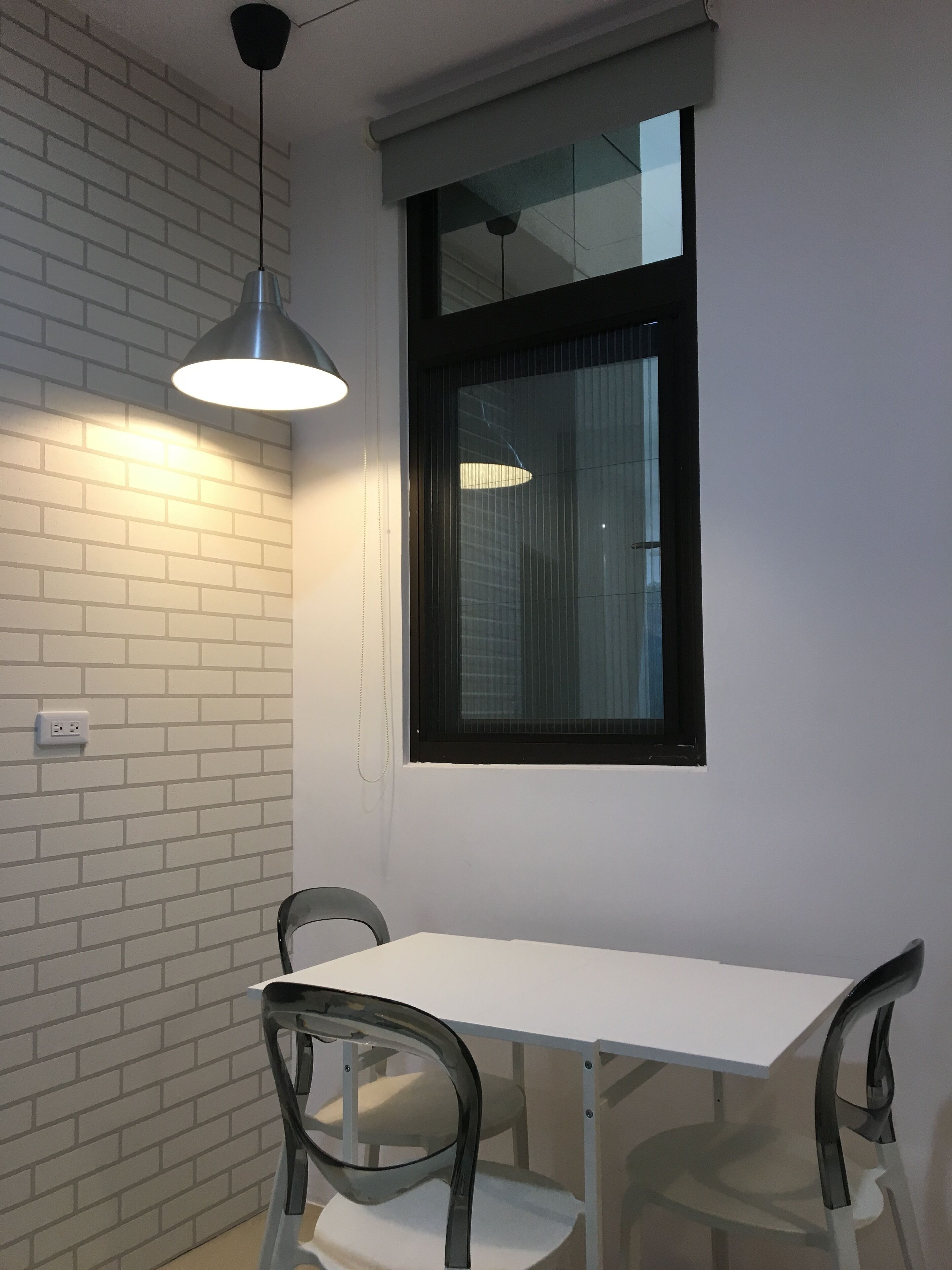 A room with a white brick wall, a window with blinds, a white table, and two chairs.