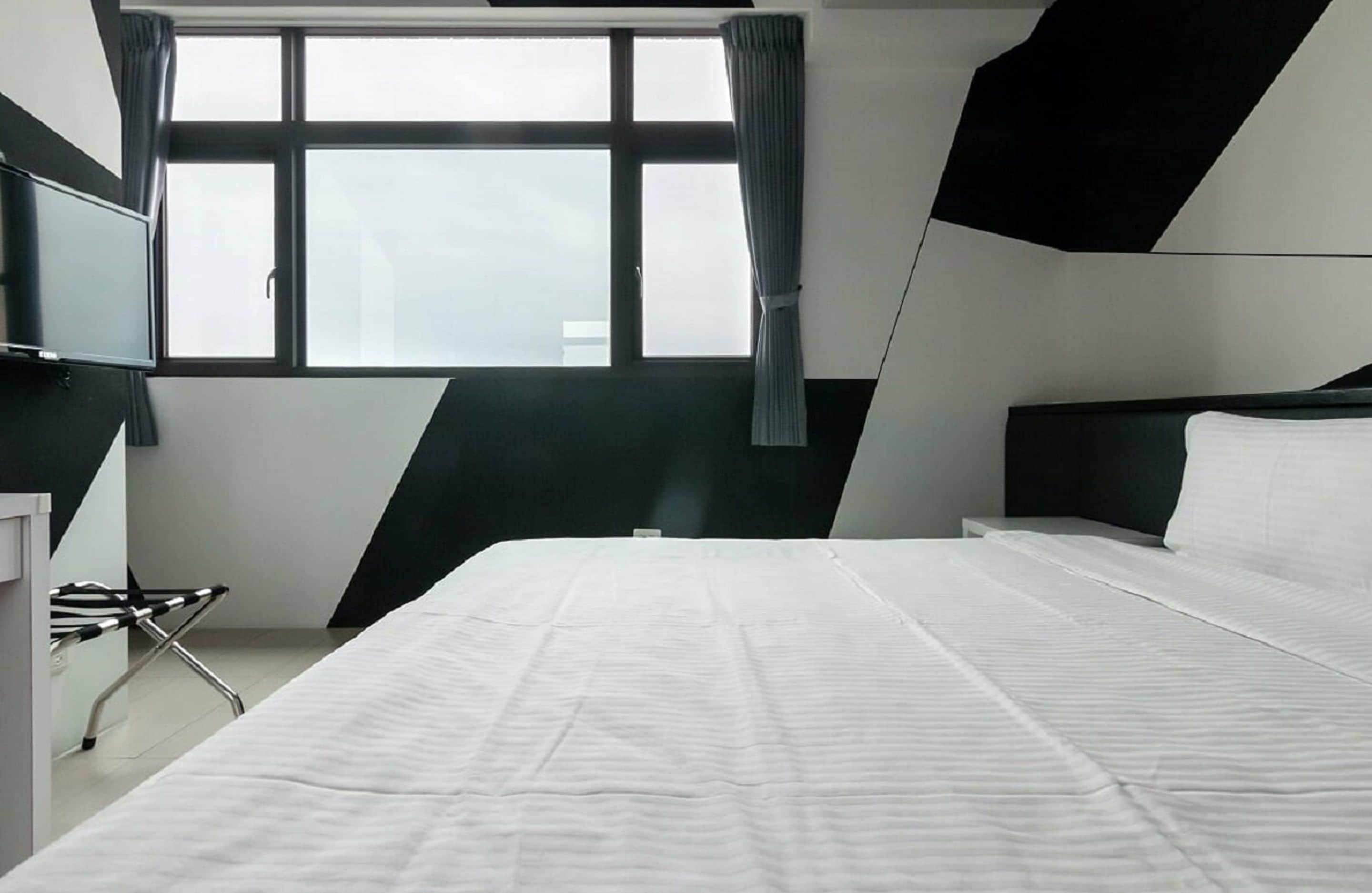 A modern hotel room with a large bed, a flat-screen TV, and a window with curtains.