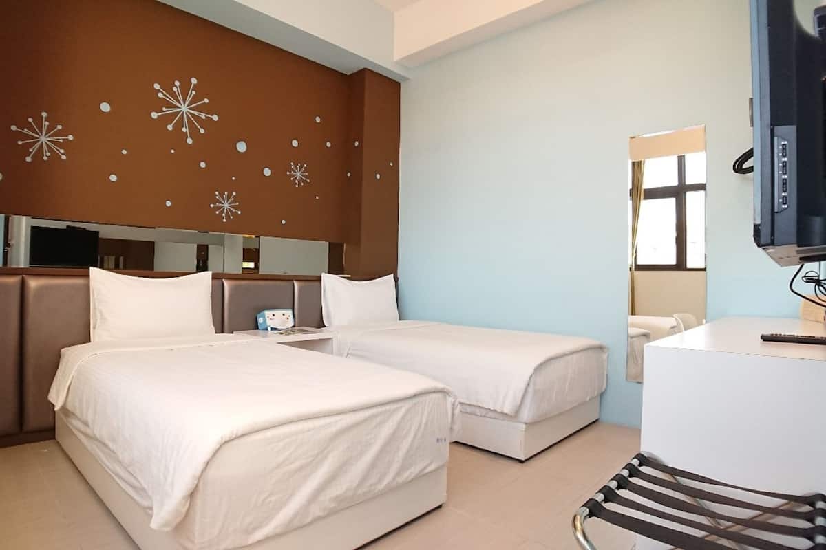 A hotel room with two beds, a desk, a chair, a TV, and a mirror.