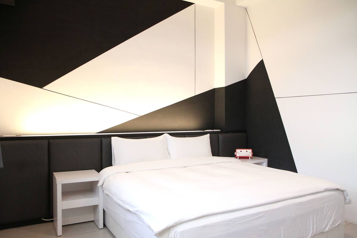 A modern bedroom with a bed, bedside tables, and a geometric wall design.