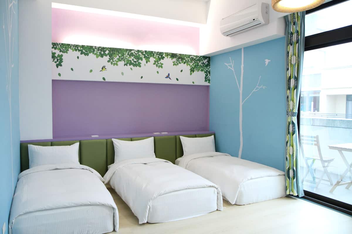 A hotel room with two beds, a purple headboard, and a view of the outside balcony.