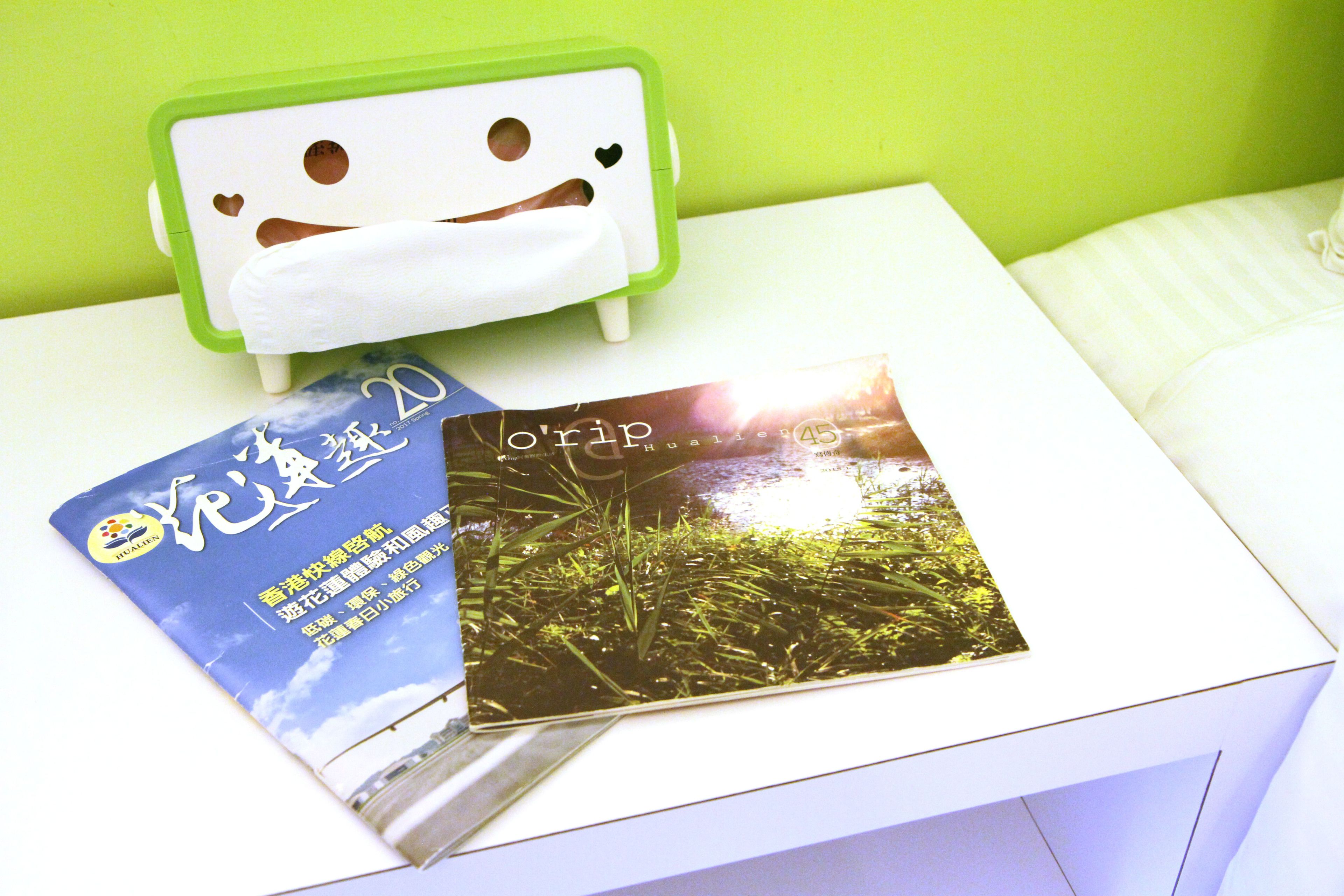 A white bedside table with a green and white nightstand, a book, and a photo album.