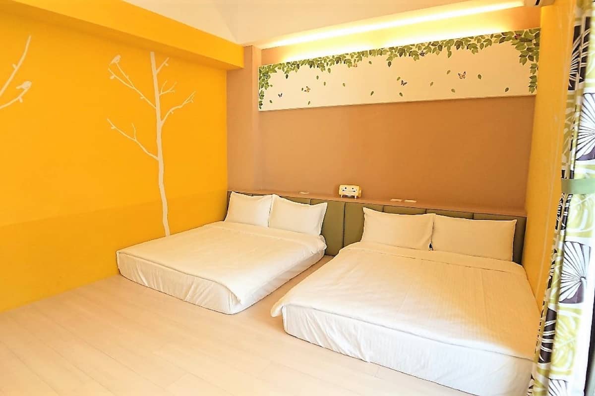 A room with two beds, a wooden floor, and a wall with a tree and butterfly mural.