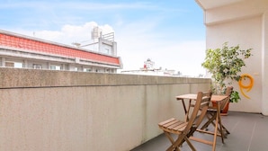 A balcony with a concrete wall, a wooden table and chairs, a potted plant, and a view of a building with a red roof. - Keyinn Space (Hualien City)