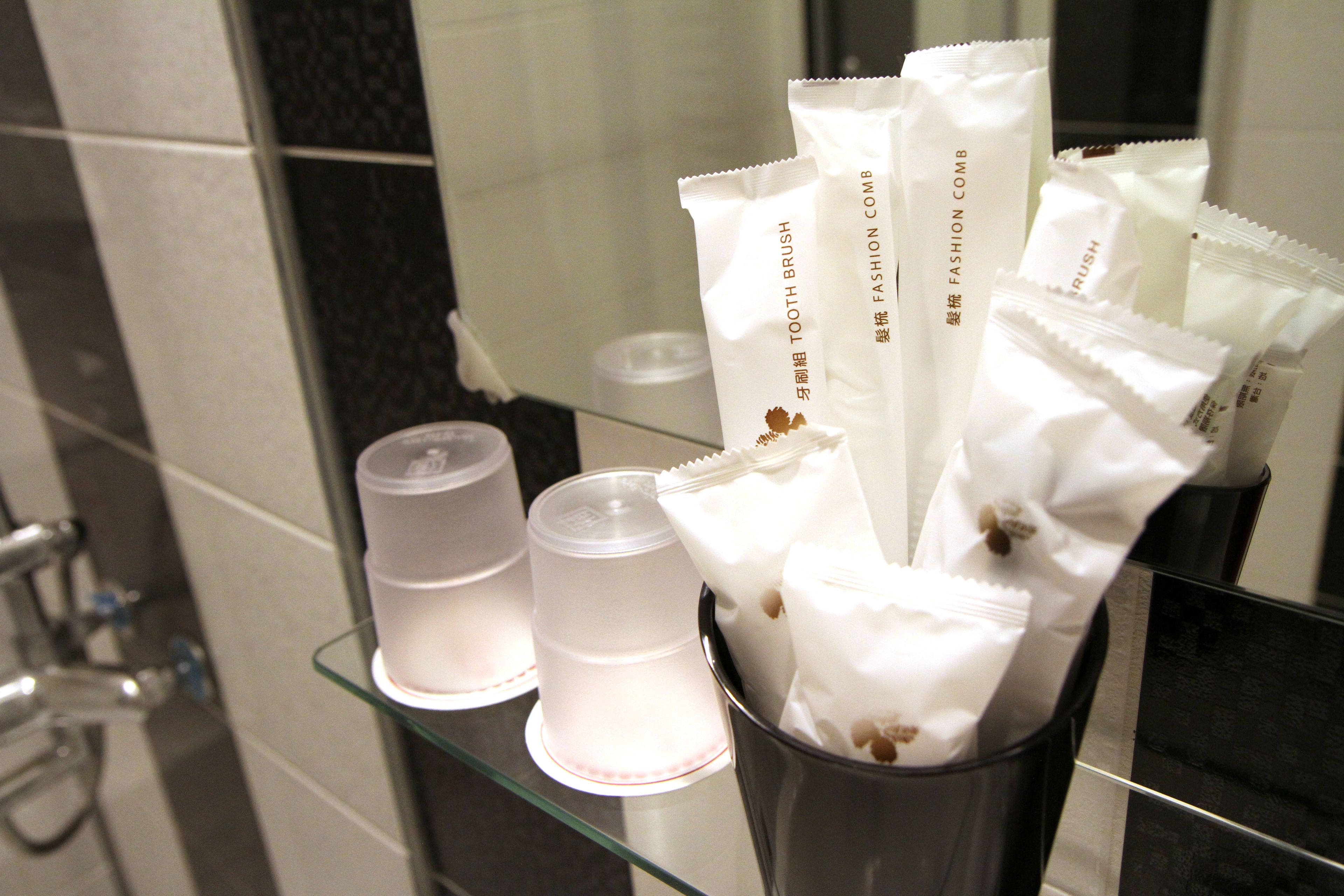 A bathroom with a glass shelf holding a toothbrush and a cup.