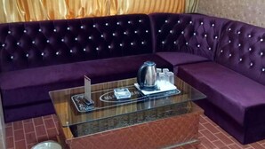 Un sofá morado con una mesita de vidrio, una tetera y tazas sobre la mesa, y un cubo de basura en el suelo.