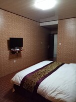 A hotel room with a bed, a flat-screen TV mounted on the wall, and a door leading to another room.