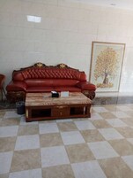 A red leather sofa and a wooden coffee table in a room with a tiled floor and a framed picture on the wall.
