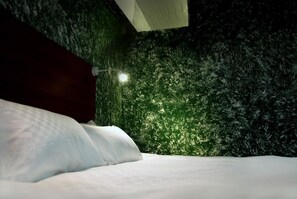 A bed with white bedding in a room with a green textured wall and a dark wooden headboard.