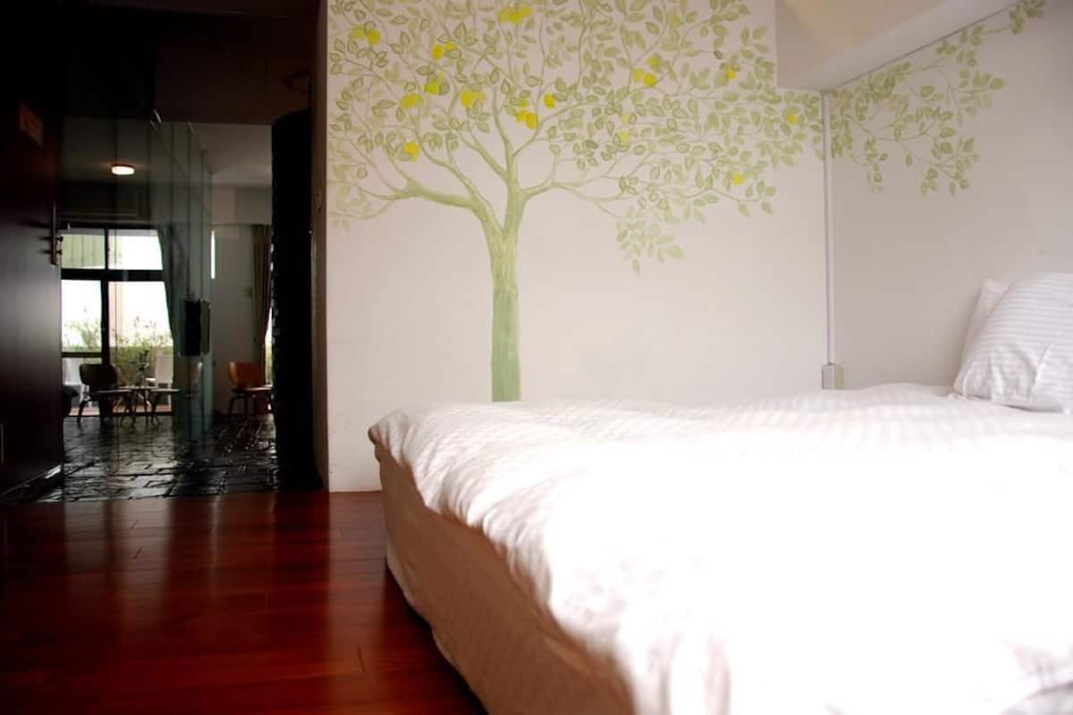 A bedroom with a bed, a wall mural of a tree, and a view of a dining area.