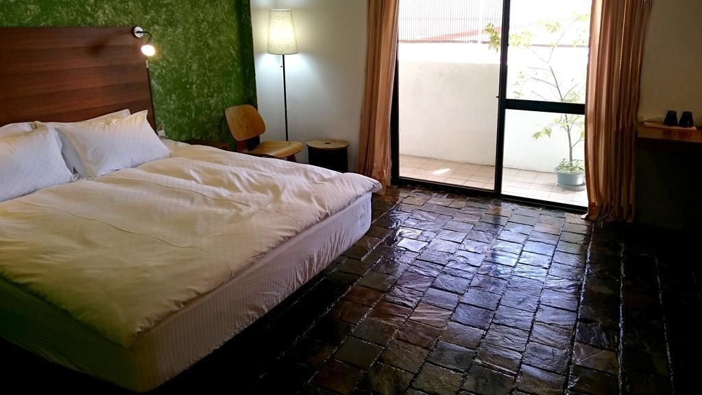 A room with a bed, a chair, a lamp, and a view through a glass door.