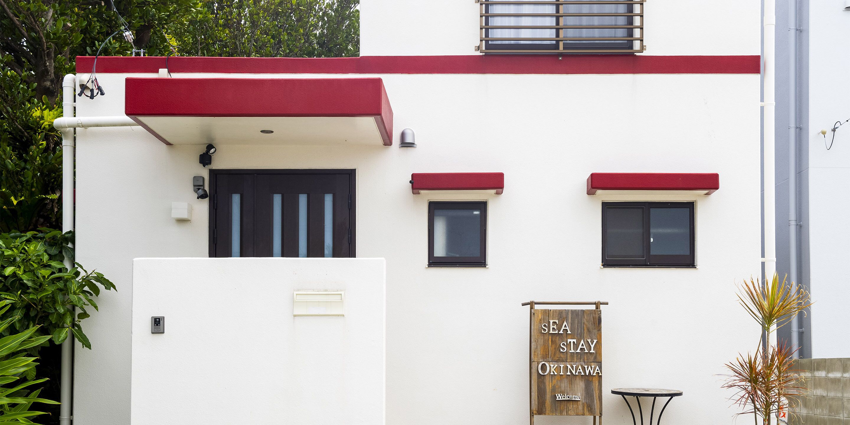 A building with a white facade, red accents, and a sign that reads "SEA STAY OKINAWA Welcome".