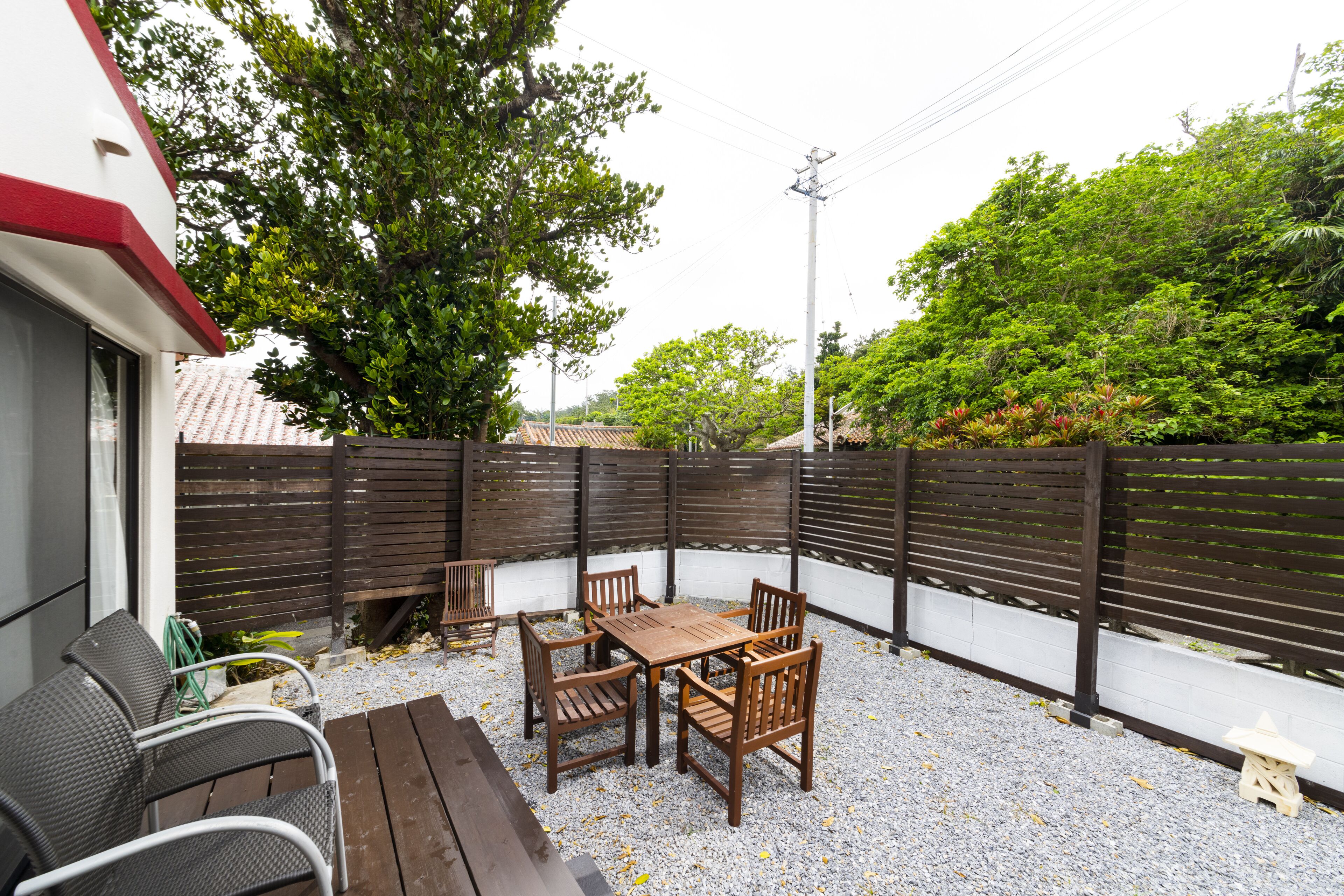 Un patio al aire libre con una mesa y sillas de madera, rodeado por un muro blanco y una valla de madera.