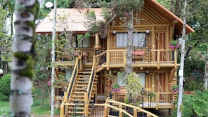 A multi-story wooden cabin with a balcony, a staircase, and a small deck area. - Hotel Britannia (Itatiaia)