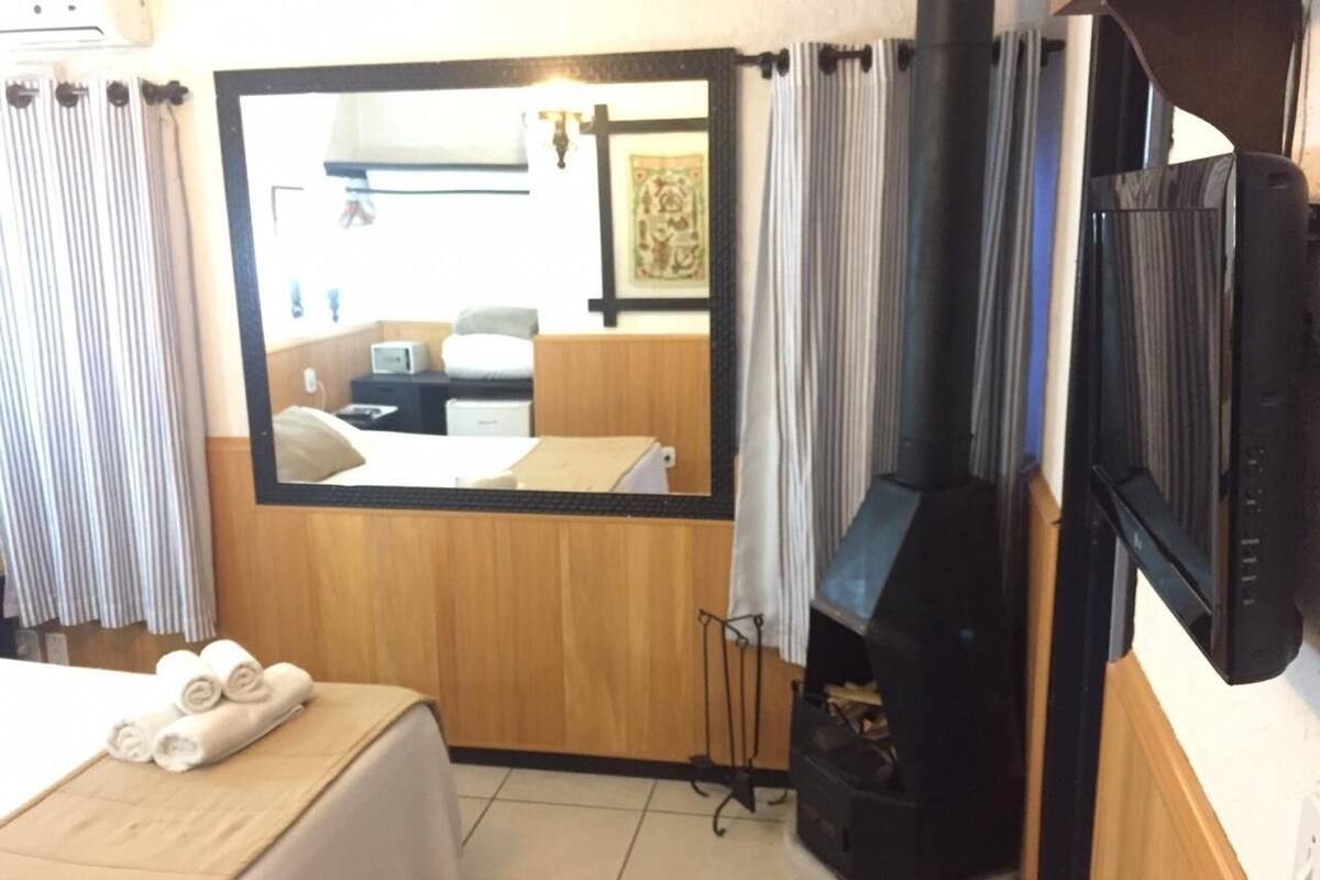 A hotel room with a bed, a TV, a small kitchenette, and a window with curtains.