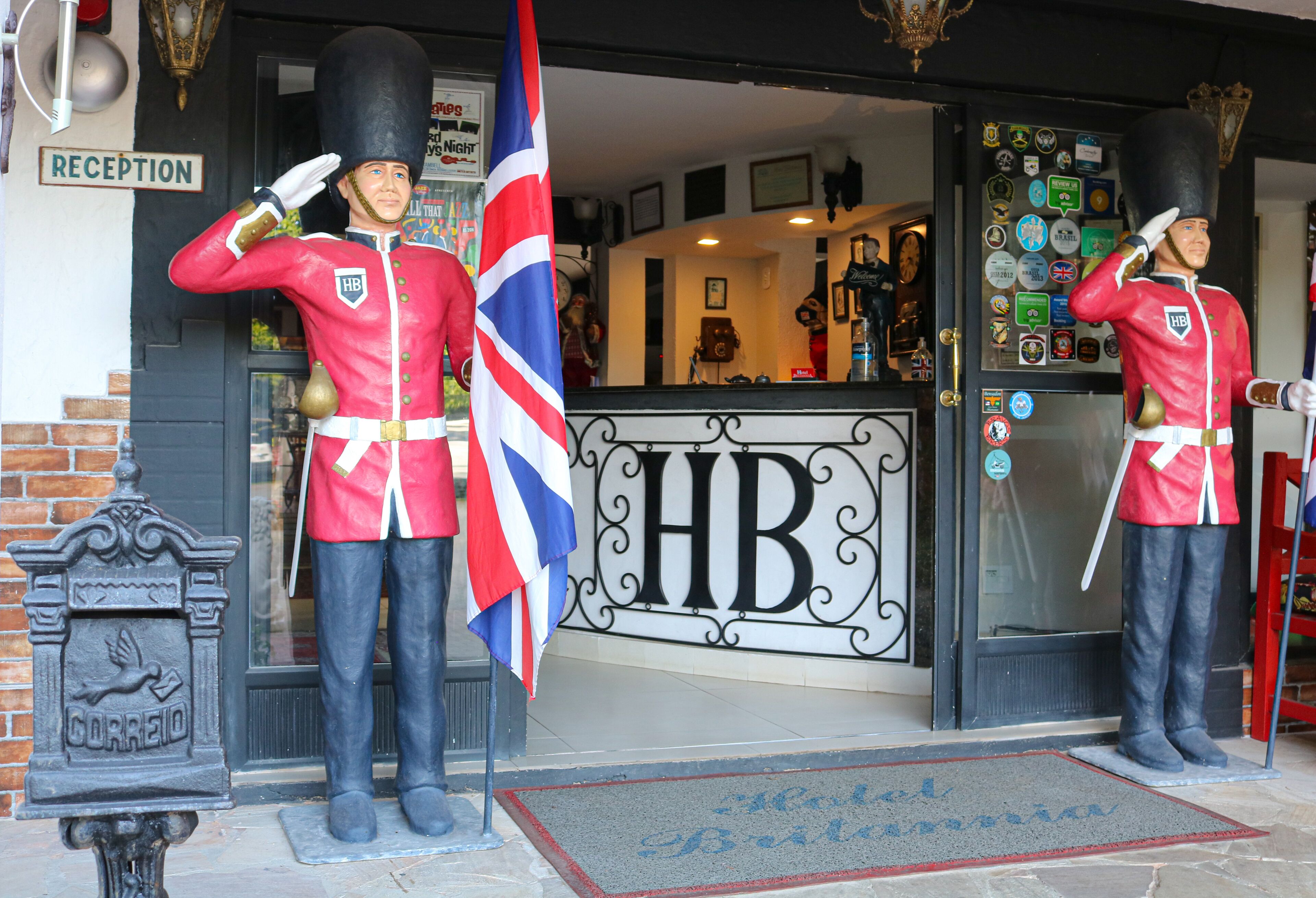 A hotel entrance with two life-sized statues of guards saluting, a reception sign, and a doormat with a welcome message.