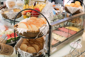 Un bufé con diferentes opciones de comida, incluyendo pan, frutas y perros calientes.