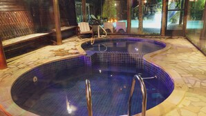 A hot tub with tiled flooring and metal railings, surrounded by wooden benches and a stone wall. - Hotel Britannia (Itatiaia)