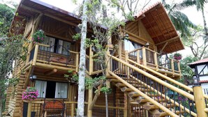 A log cabin with multiple balconies, a wooden staircase, and a porch area with flowers. - Hotel Britannia (Itatiaia)
