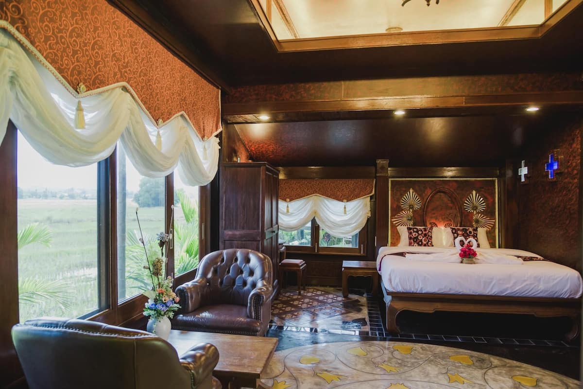 A spacious bedroom with a large bed, a leather armchair, and a view of a green field through large windows.