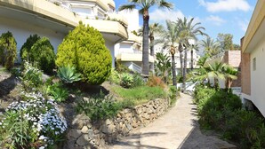 A pathway flanked by lush greenery and palm trees, leading to a building with balconies. - Bright&Large Penthouse, 2Terraces, Pools, Garden, 2 swimming Pools,Beachs, Golf (Benalmádena)