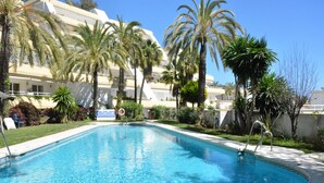 A rectangular swimming pool with clear blue water, surrounded by palm trees and a building with balconies. - Bright&Large Penthouse, 2Terraces, Pools, Garden, 2 swimming Pools,Beachs, Golf (Benalmádena)