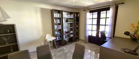 A modern room with a glass table, two chairs, a bookshelf, and a door leading outside.