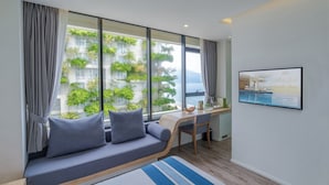 A modern room with a large window, a sofa, a desk, and a chair. - Parosand Danang Hotel (Da Nang)