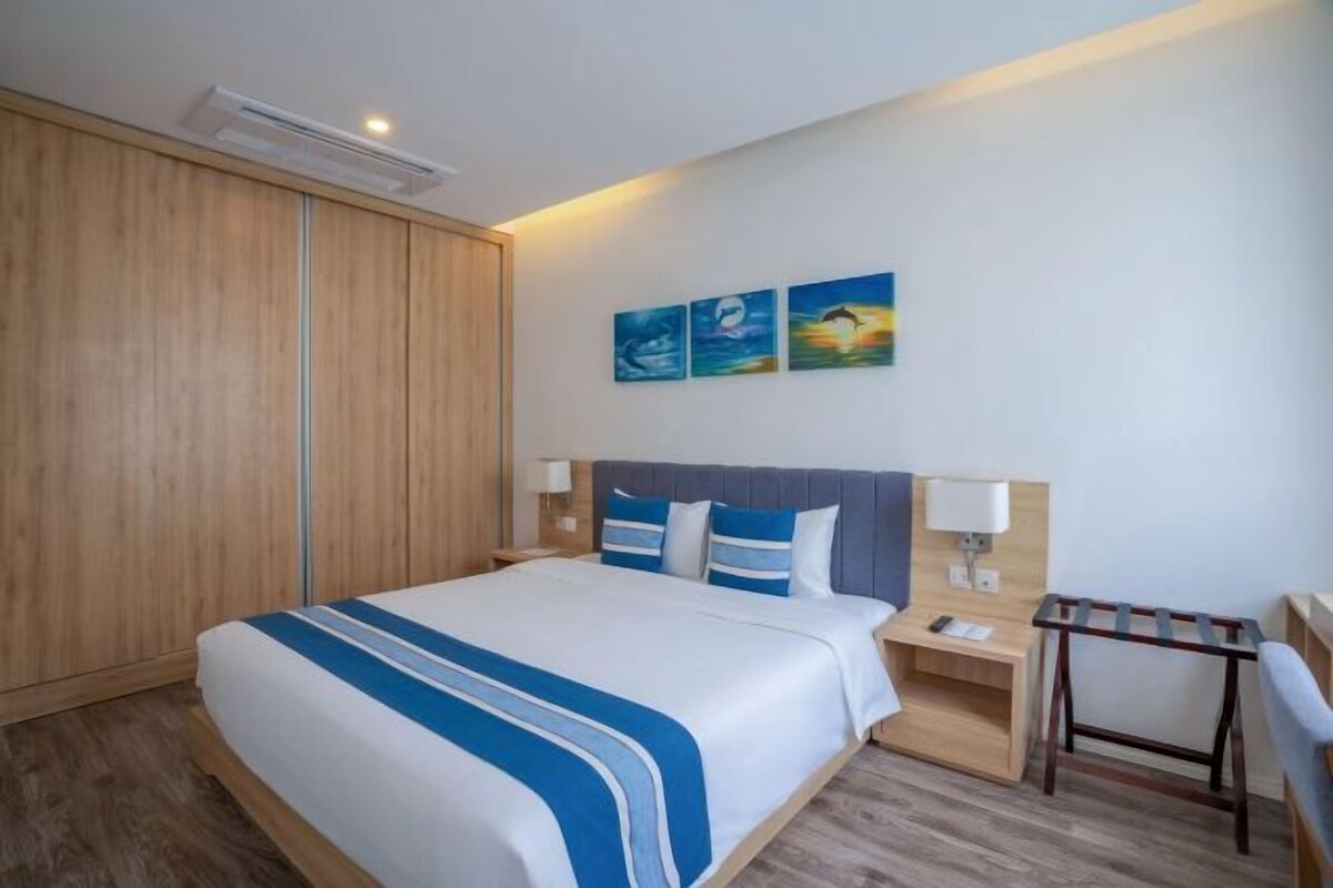 A hotel room with a bed, bedside tables, a desk, and a chair. There are three paintings on the wall.