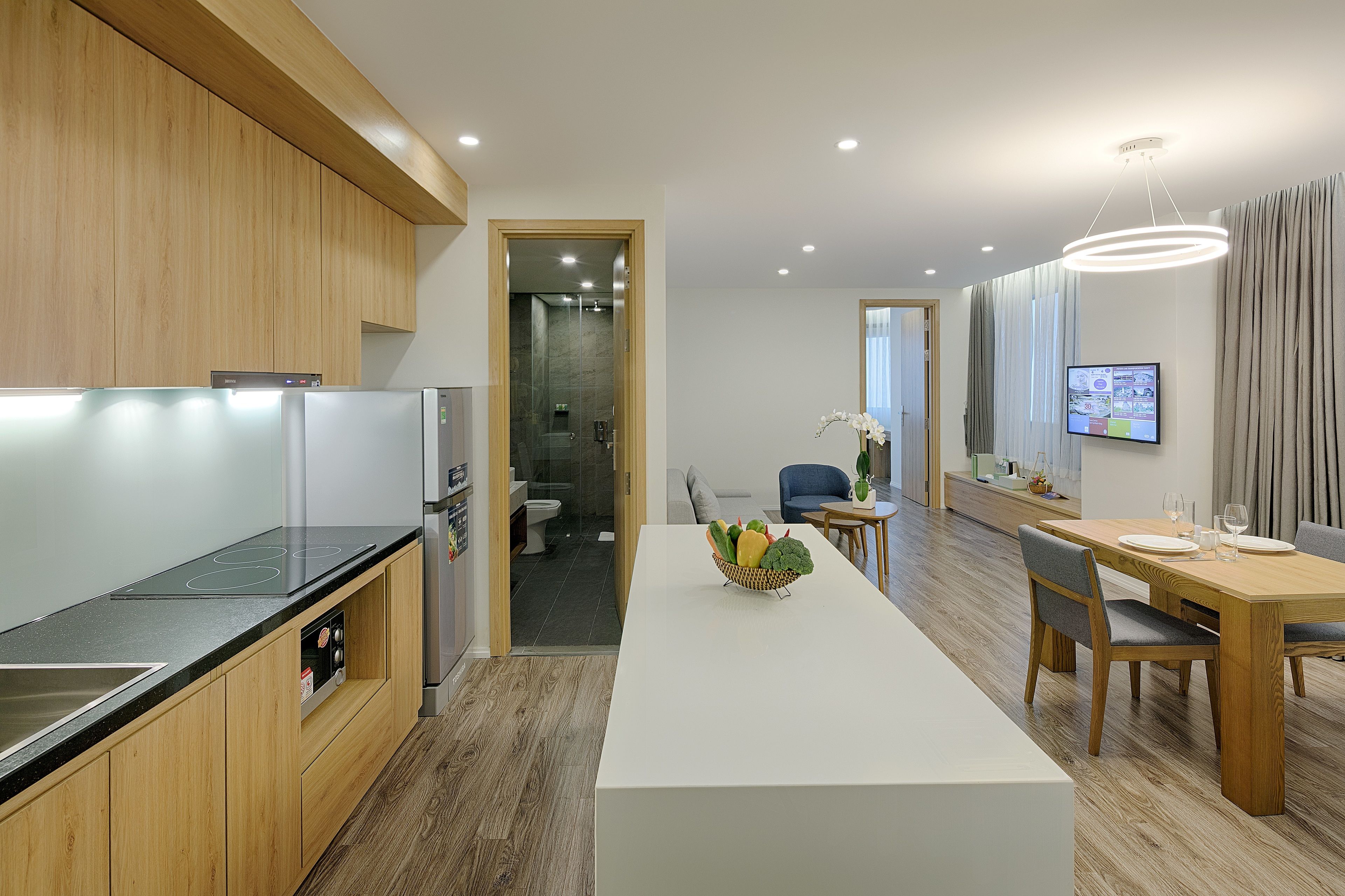 Une cuisine moderne avec des meubles en bois et un four encastré, un coin repas avec une table et des chaises en bois, et un espace de vie avec un téléviseur et des rideaux.