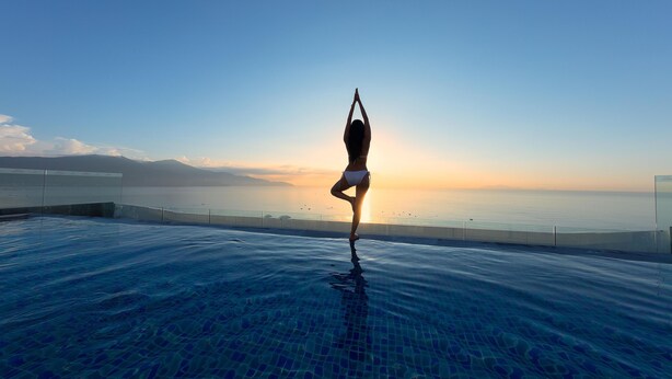 A person performing a yoga pose on a pool deck with a sunset view. - Parosand Danang Hotel (Da Nang)
