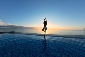 A person performing a yoga pose on a pool deck with a sunset view. - Parosand Danang Hotel (Da Nang)