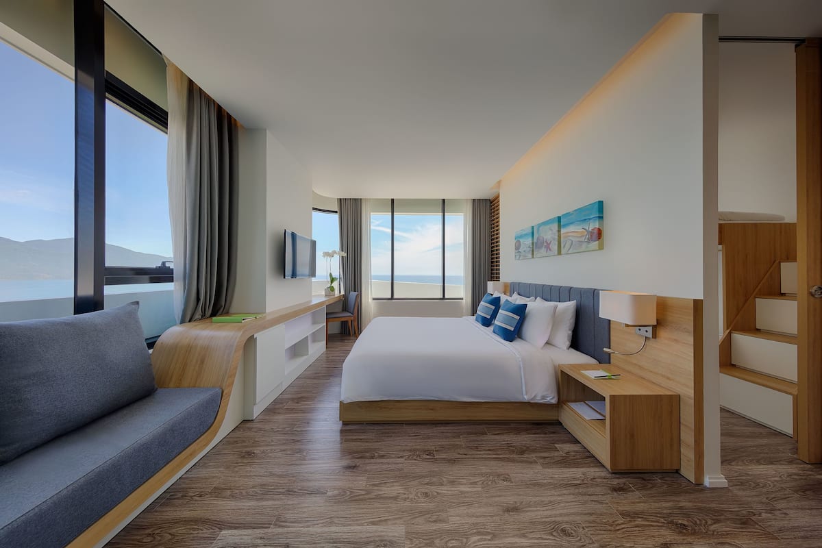 A modern hotel room with a large bed, a sofa, a desk, and a TV.