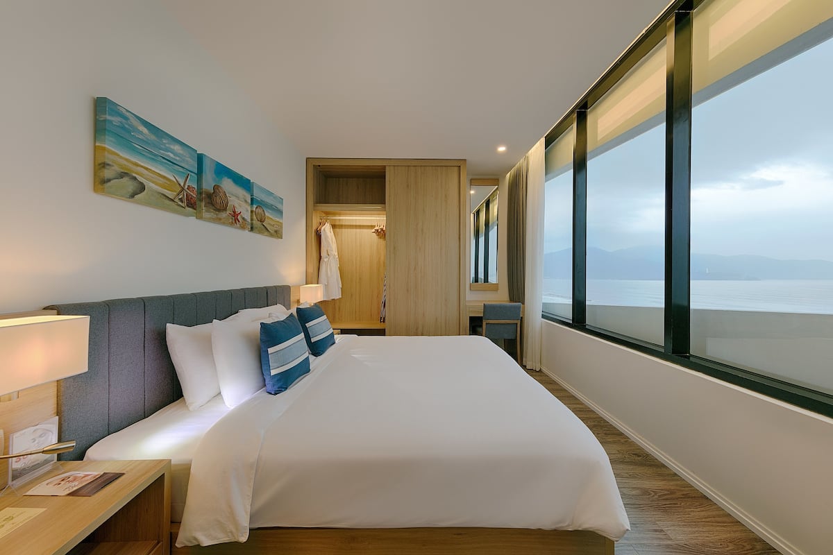 A hotel room with a large bed, a desk, a wardrobe, and a view of the sea.