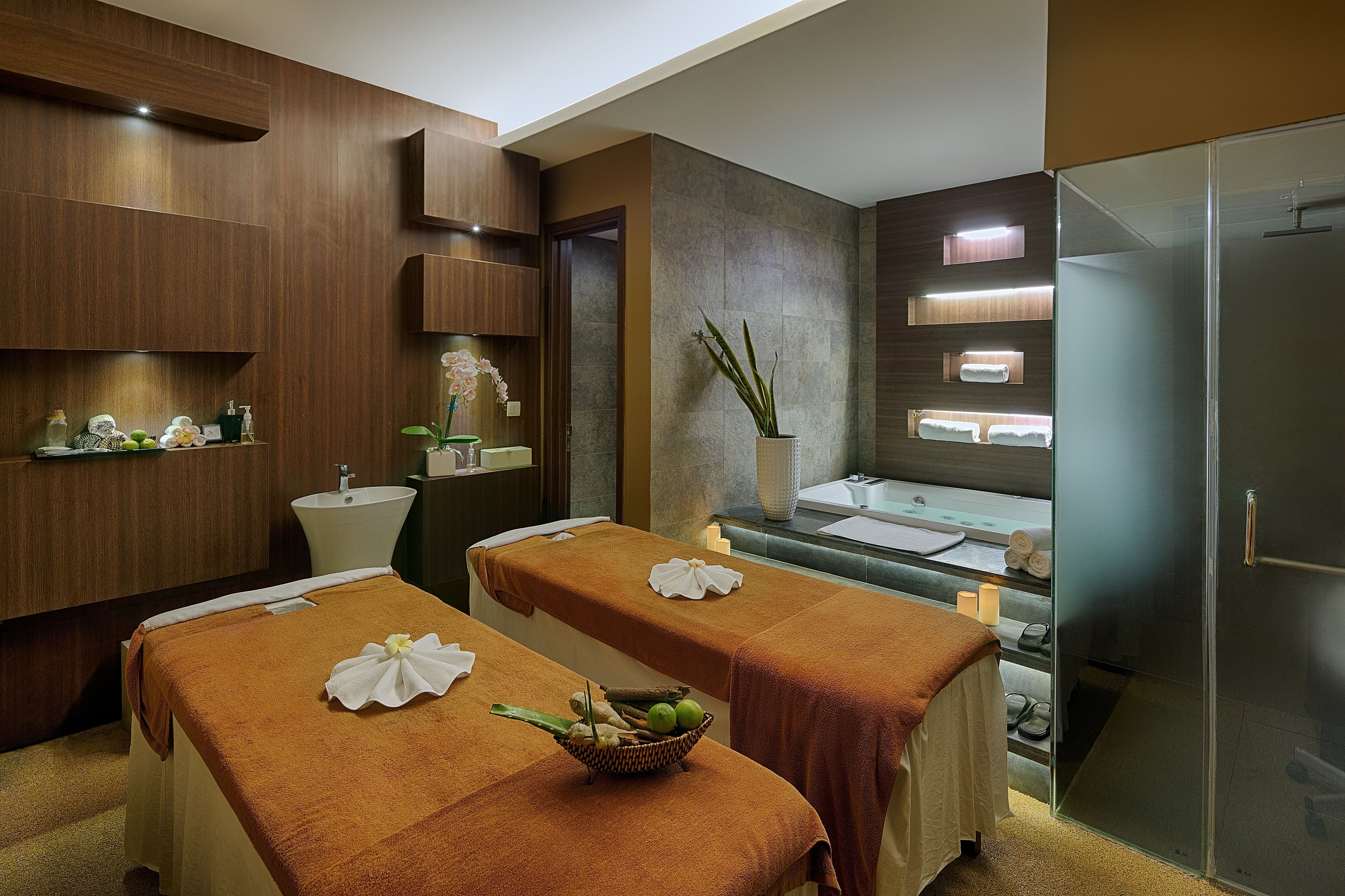 A modern spa room with two massage tables, a sink, and a glass shower enclosure.