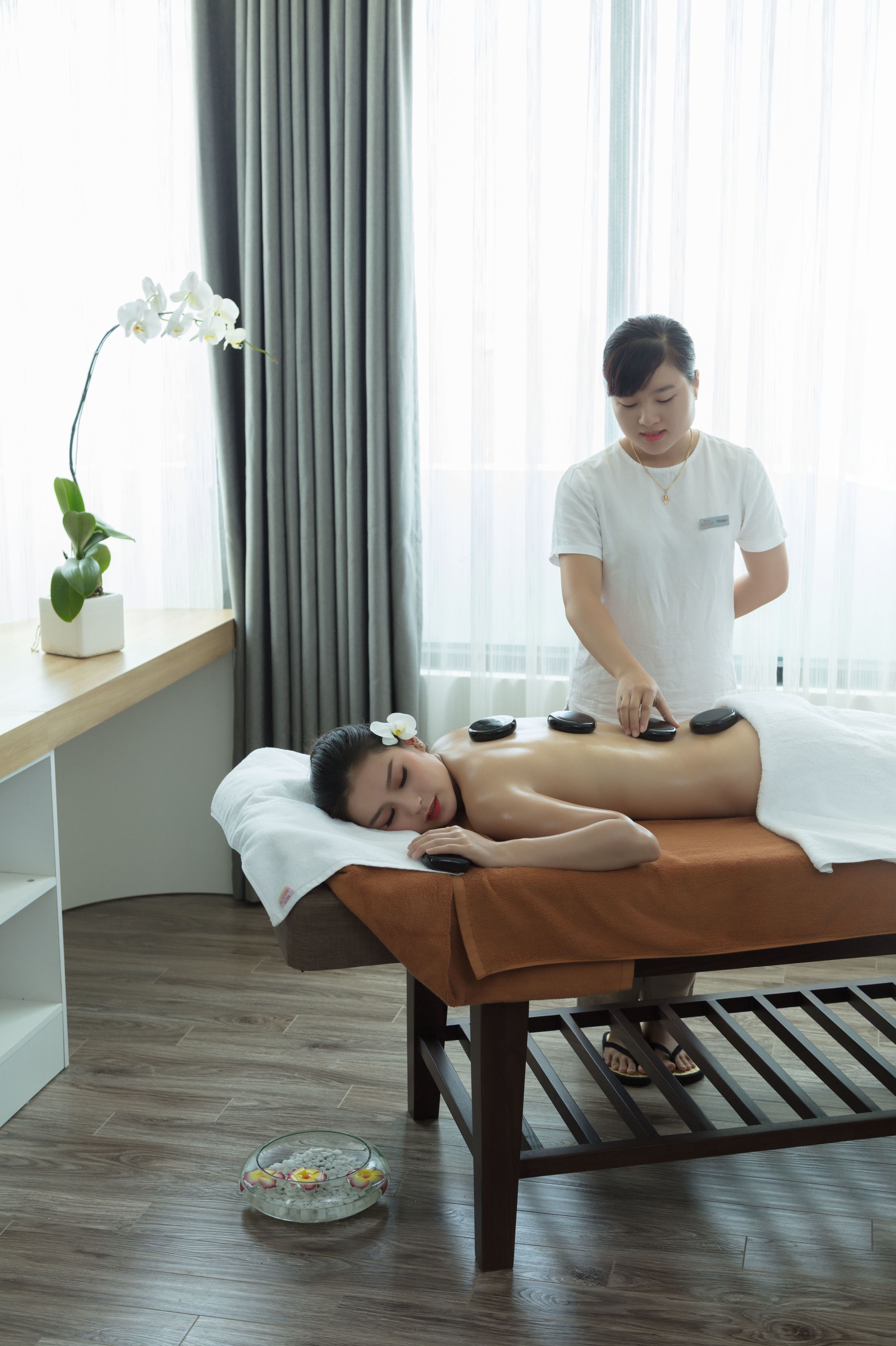 A massage therapy session in a room with a wooden floor, a massage table, and a potted orchid.