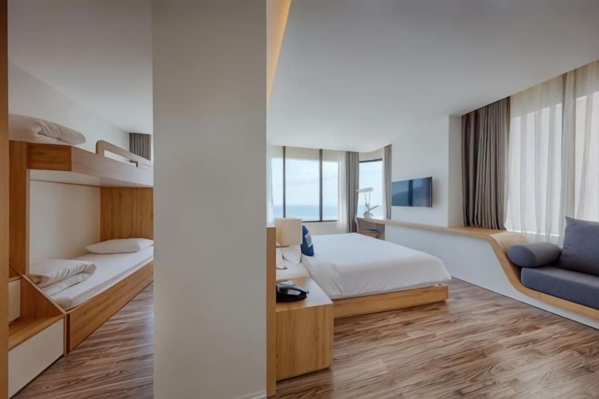 Une chambre d’hôtel moderne équipée d’un lit superposé, d’un lit simple, d’un canapé, d’une télévision et d’une grande fenêtre.
