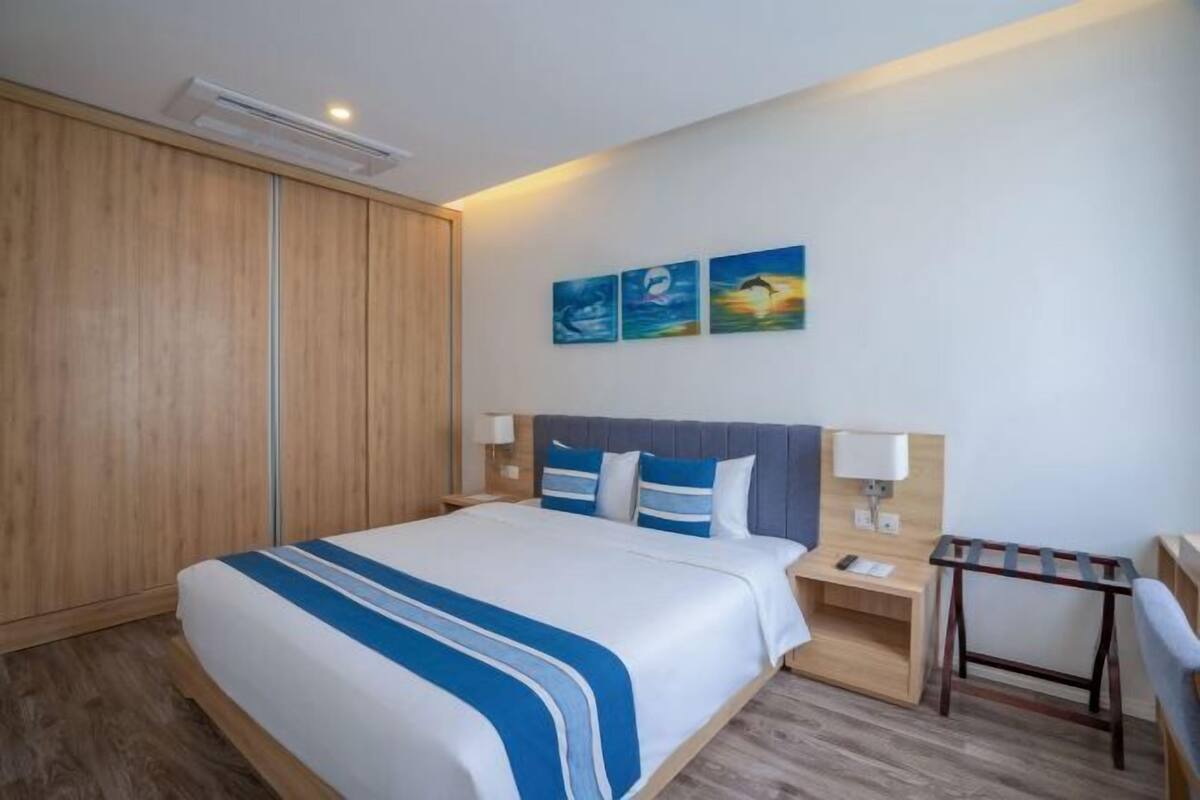 A hotel room with a bed, bedside tables, a desk, and a chair. There are three paintings on the wall.