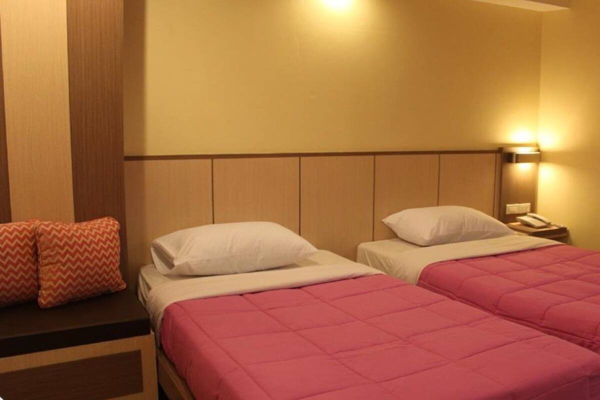 Camera d'albergo con due letti, ognuno con una coperta rosa e cuscini bianchi. C'è un comodino con un telefono e una lampada.