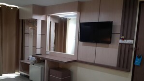 A hotel room with a vanity area, a television mounted on the wall, and a small refrigerator.