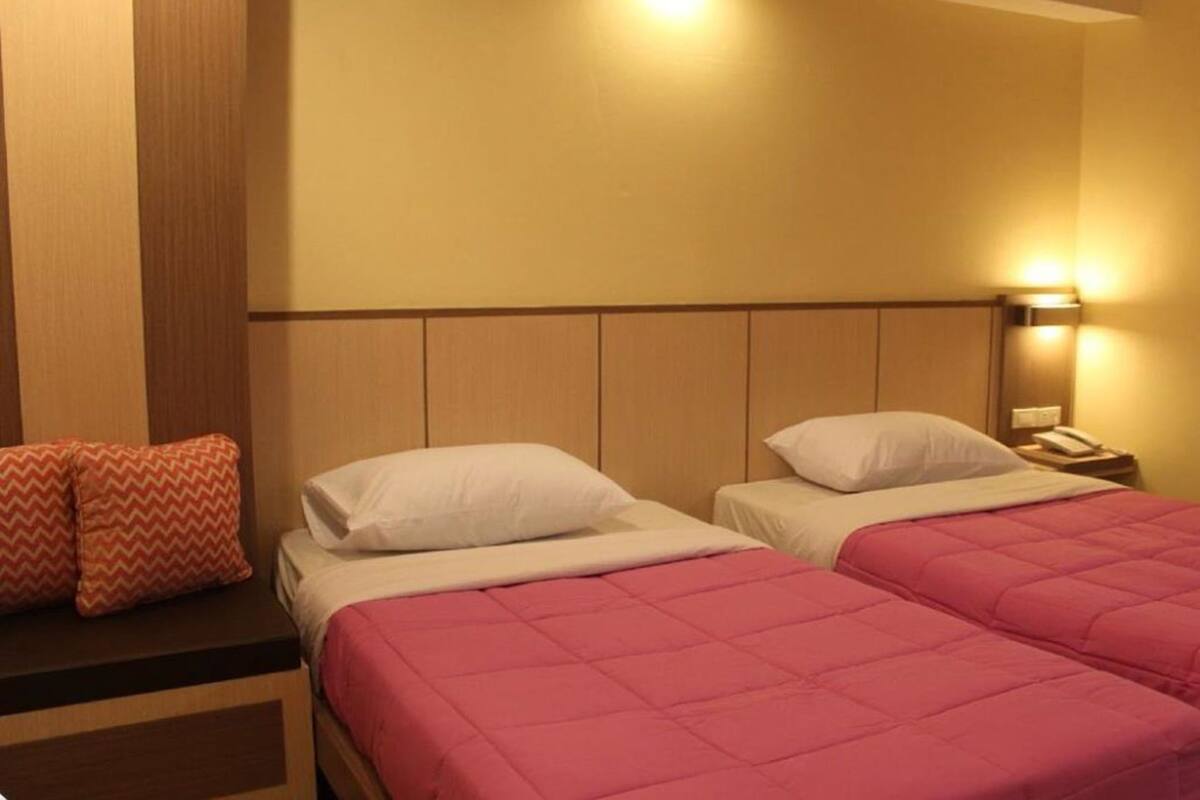 Una camera d'albergo con due letti, un comodino e una lampada a parete.