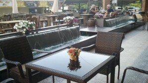 An outdoor seating area with wicker chairs and a glass table, a water feature, and a flower vase.