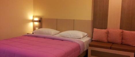 A bedroom with a bed, a nightstand, a wall-mounted light, and a wooden panel wall.